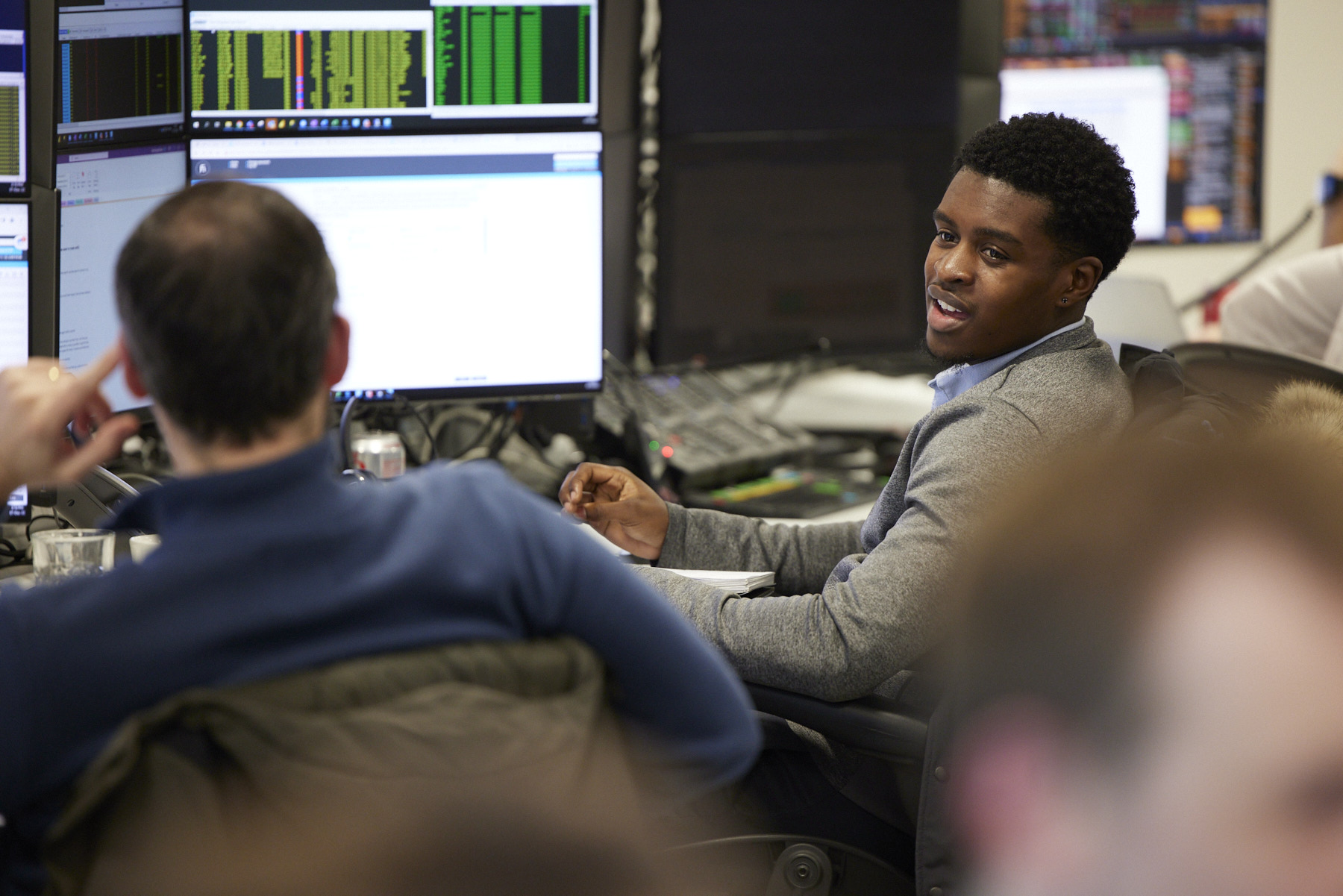 Black male banker working with other bankers in front of computer monitor in an open office.