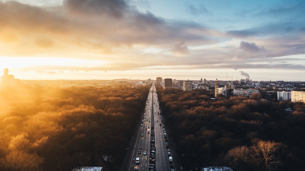 Aerial view of large roadway with tree scenery and a cityscape in view with beautiful sky